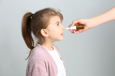 Photo of Mother helping her daughter to use nasal spray on white background