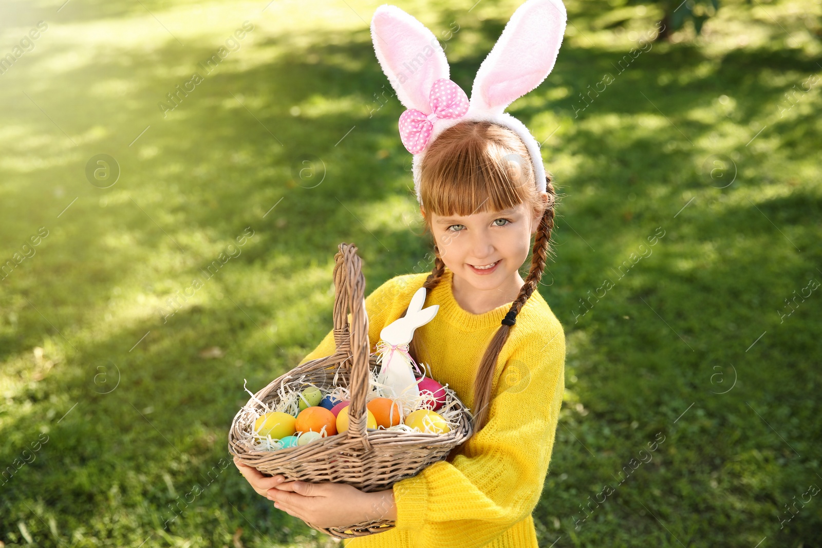 Photo of Cute little girl with bunny ears and basket of Easter eggs in park