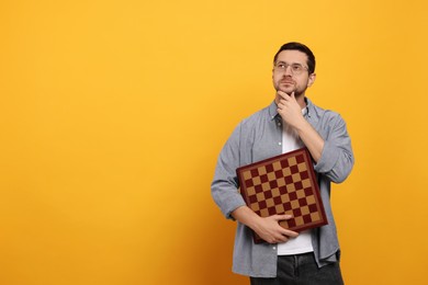 Photo of Thoughtful man holding chessboard on orange background. Space for text