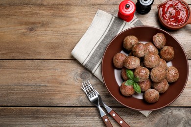 Tasty cooked meatballs with basil served on wooden table, flat lay. Space for text