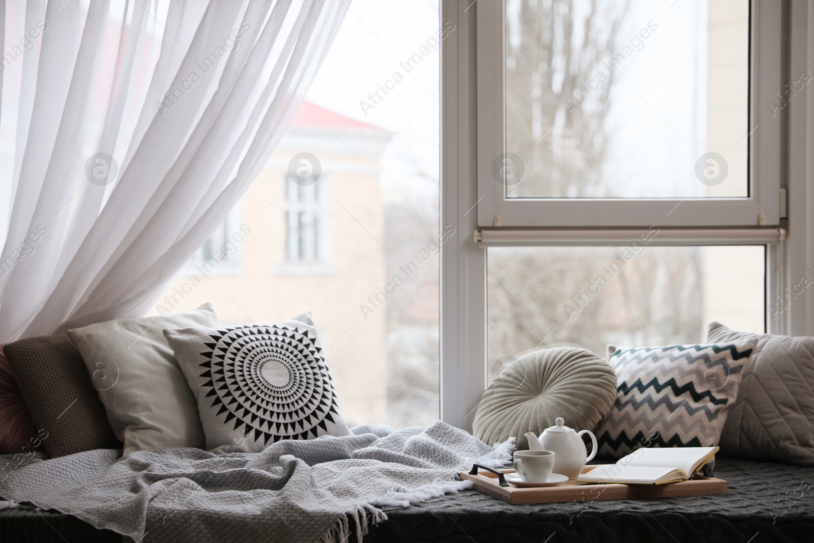 Photo of Comfortable lounge area with blanket and soft pillows near window in room