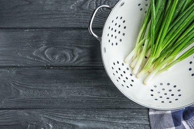 Colander with fresh green onion on wooden table, top view