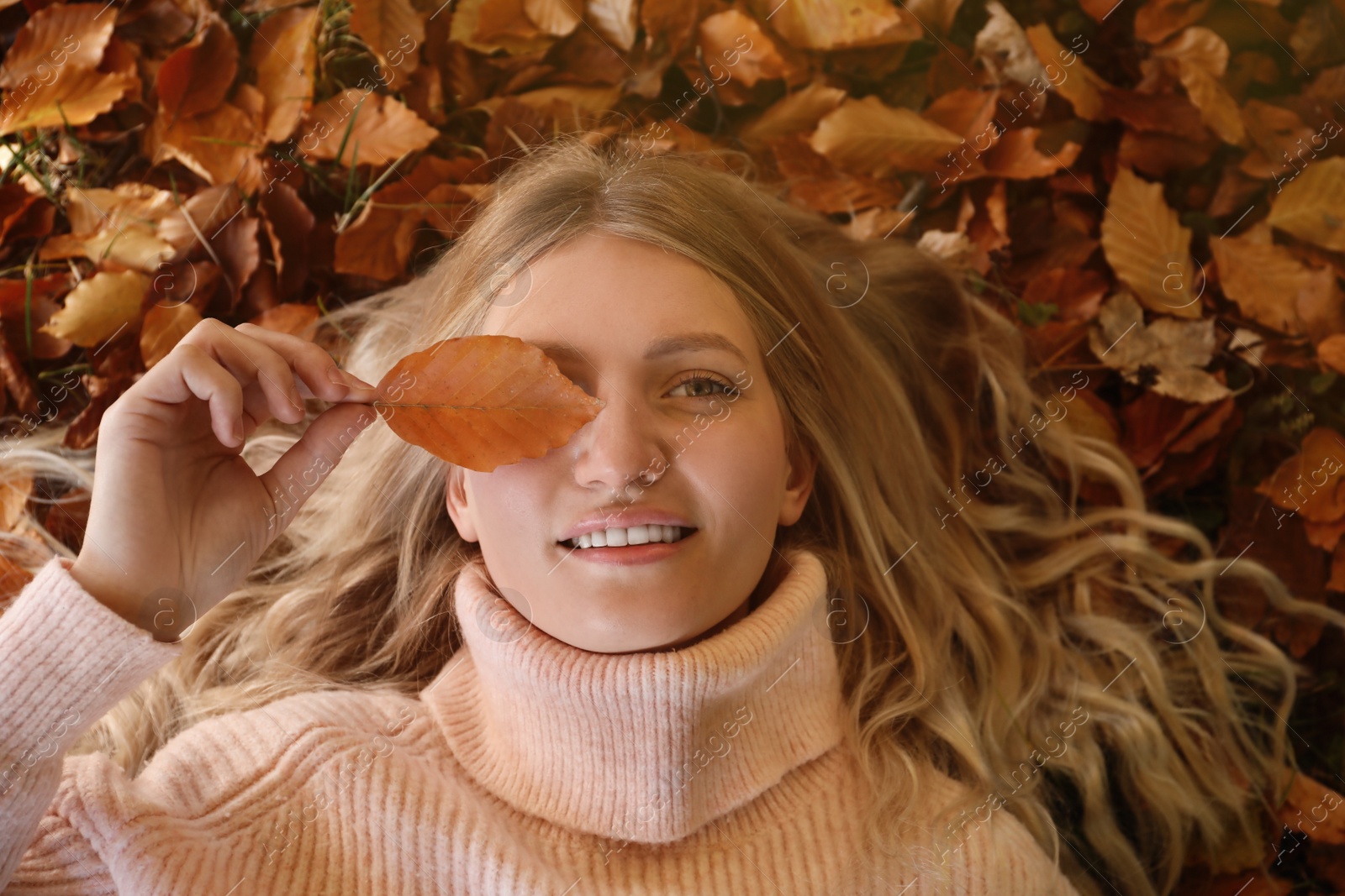 Photo of Portrait of beautiful young woman lying in autumn leaves, top view