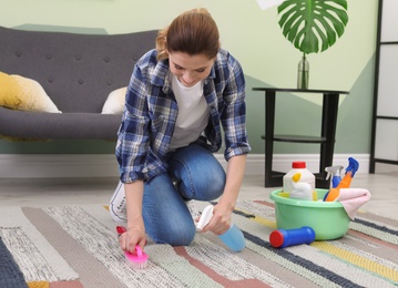 Photo of Woman cleaning carpet with brush at home