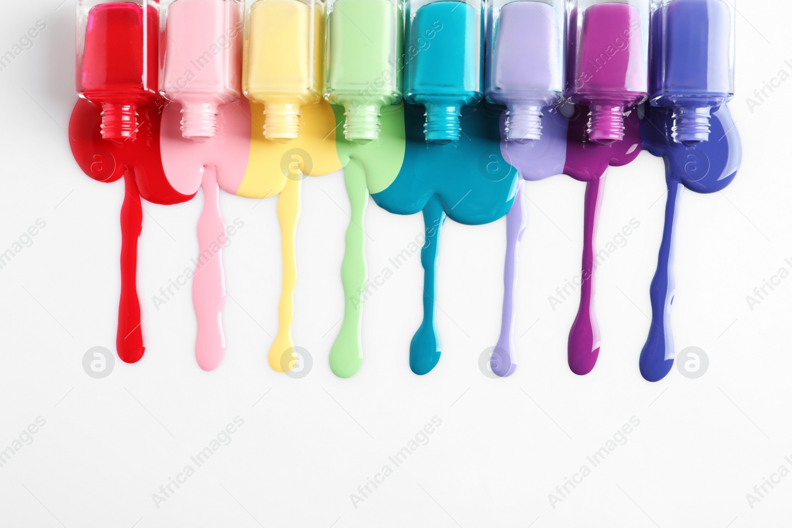 Photo of Spilled colorful nail polishes and bottles on white background, top view