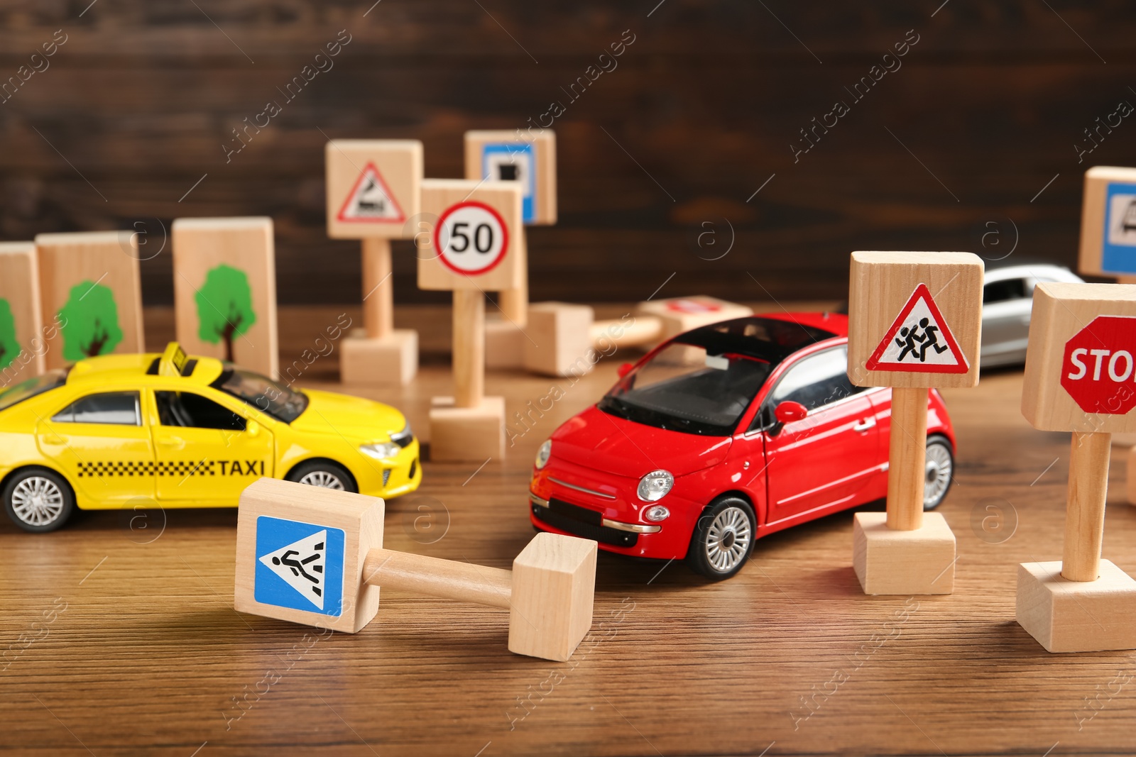 Photo of Different miniature road signs and cars on wooden table. Driving school