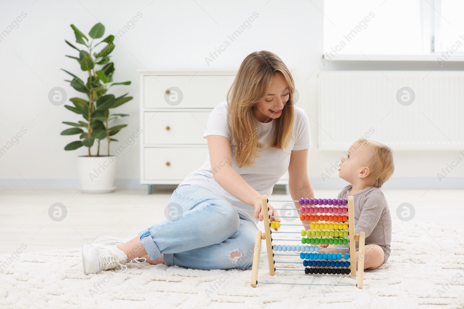 Photo of Children toys. Happy mother and her little son playing with wooden abacus on rug at home