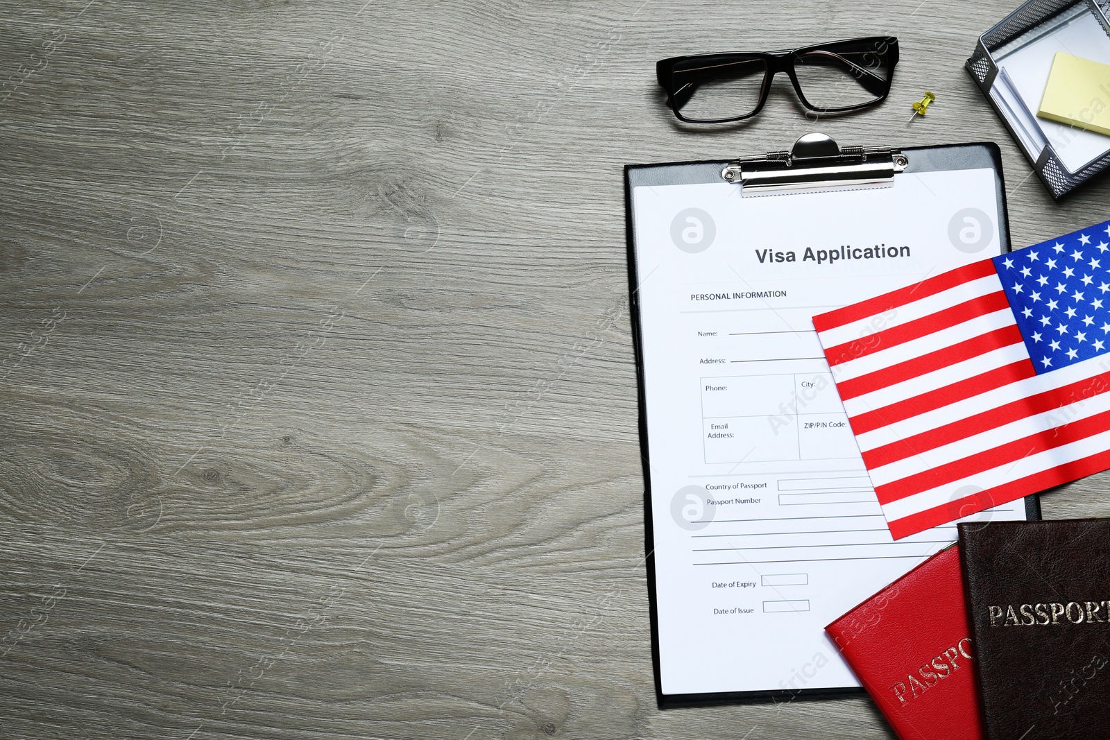 Photo of Visa application form, American flag, passports and stationery on wooden table, flat lay. Space for text