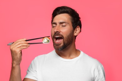 Handsome man eating tasty sushi roll with chopsticks on pink background