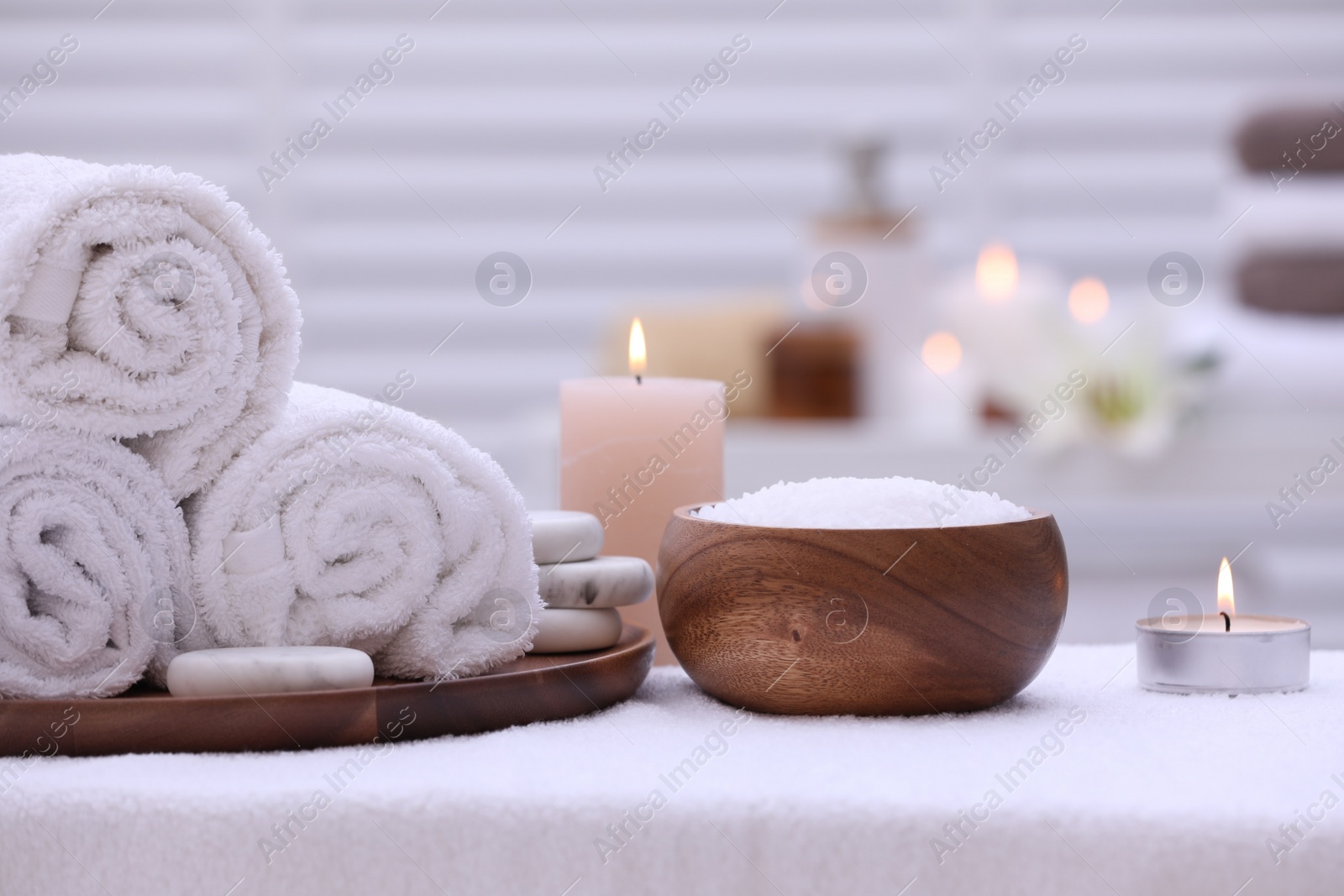 Photo of Spa composition with rolled towels and burning candles on massage table in wellness center