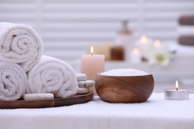 Spa composition with rolled towels and burning candles on massage table in wellness center