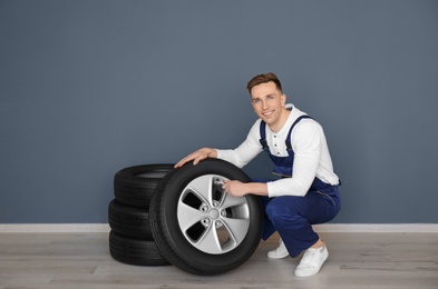 Male mechanic with car tires on grey wall background