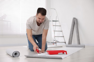 Man applying glue onto wallpaper sheet in room