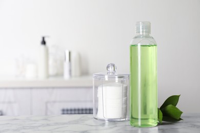 Photo of Cotton pads, leaves and makeup removal product on white marble table in bathroom. Space for text