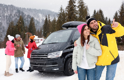 Photo of Happy couple and their friends near car on snowy road. Winter vacation