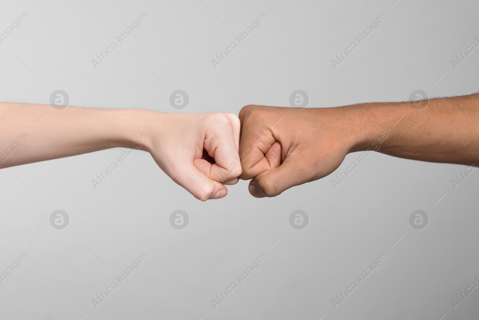 Photo of International relationships. People making fist bump on light grey background, closeup