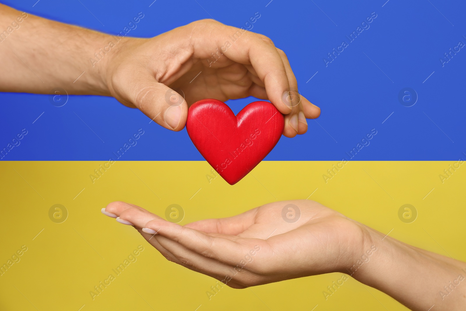 Image of Man giving woman red heart with Ukrainian flag on background, closeup. Volunteering during war