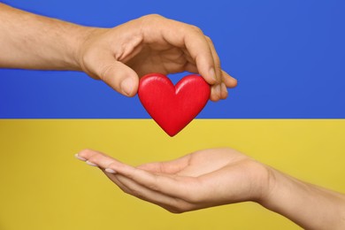 Image of Man giving woman red heart with Ukrainian flag on background, closeup. Volunteering during war