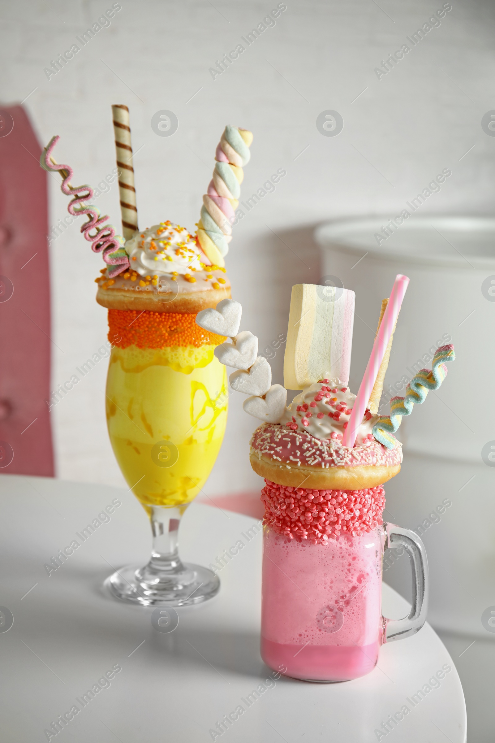 Photo of Tasty milk shakes with sweets in glassware on table at cafe