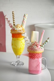 Photo of Tasty milk shakes with sweets in glassware on table at cafe