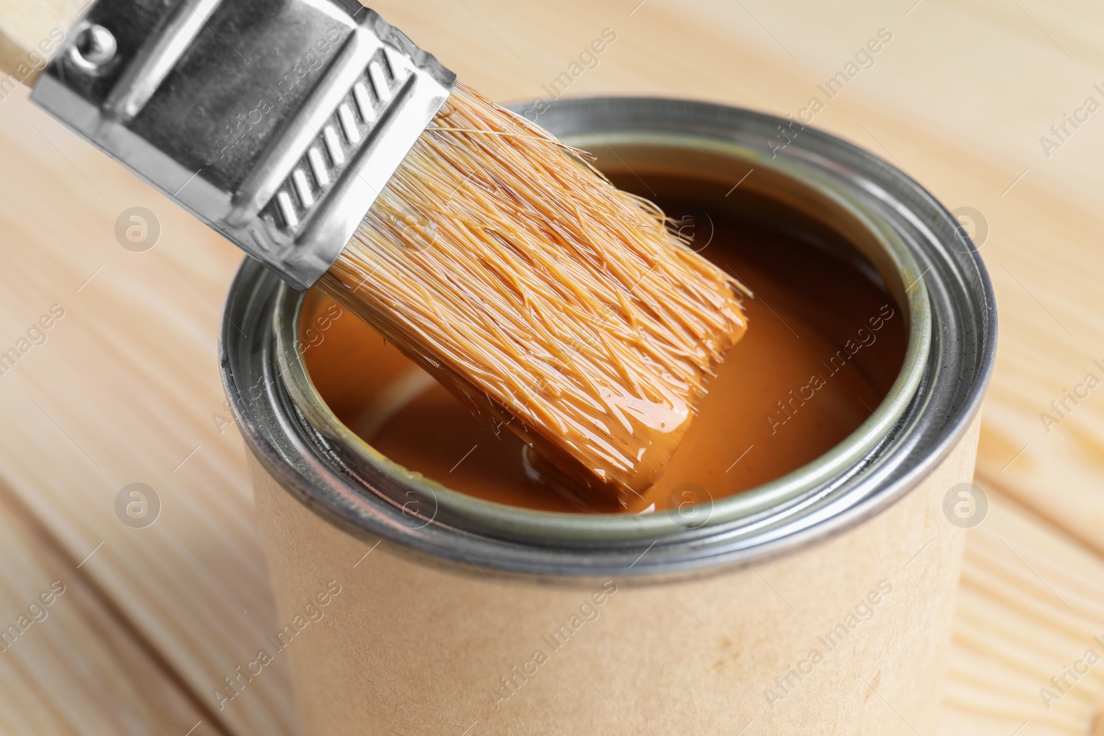 Photo of Dipping brush into can with wood stain on wooden surface, closeup