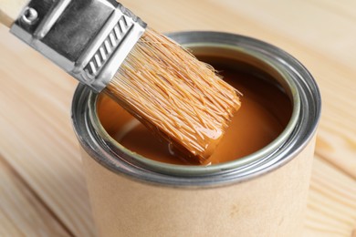 Photo of Dipping brush into can with wood stain on wooden surface, closeup