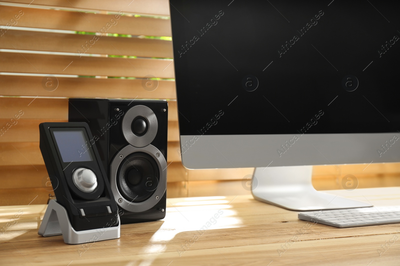 Photo of Modern computer with audio speaker and remote on wooden table indoors