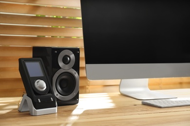 Photo of Modern computer with audio speaker and remote on wooden table indoors