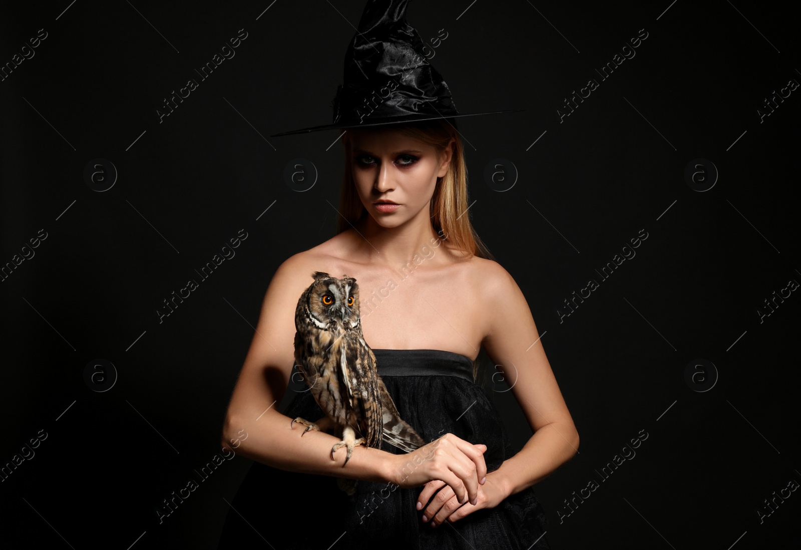 Photo of Witch in black hat with owl on dark background. Scary fantasy character