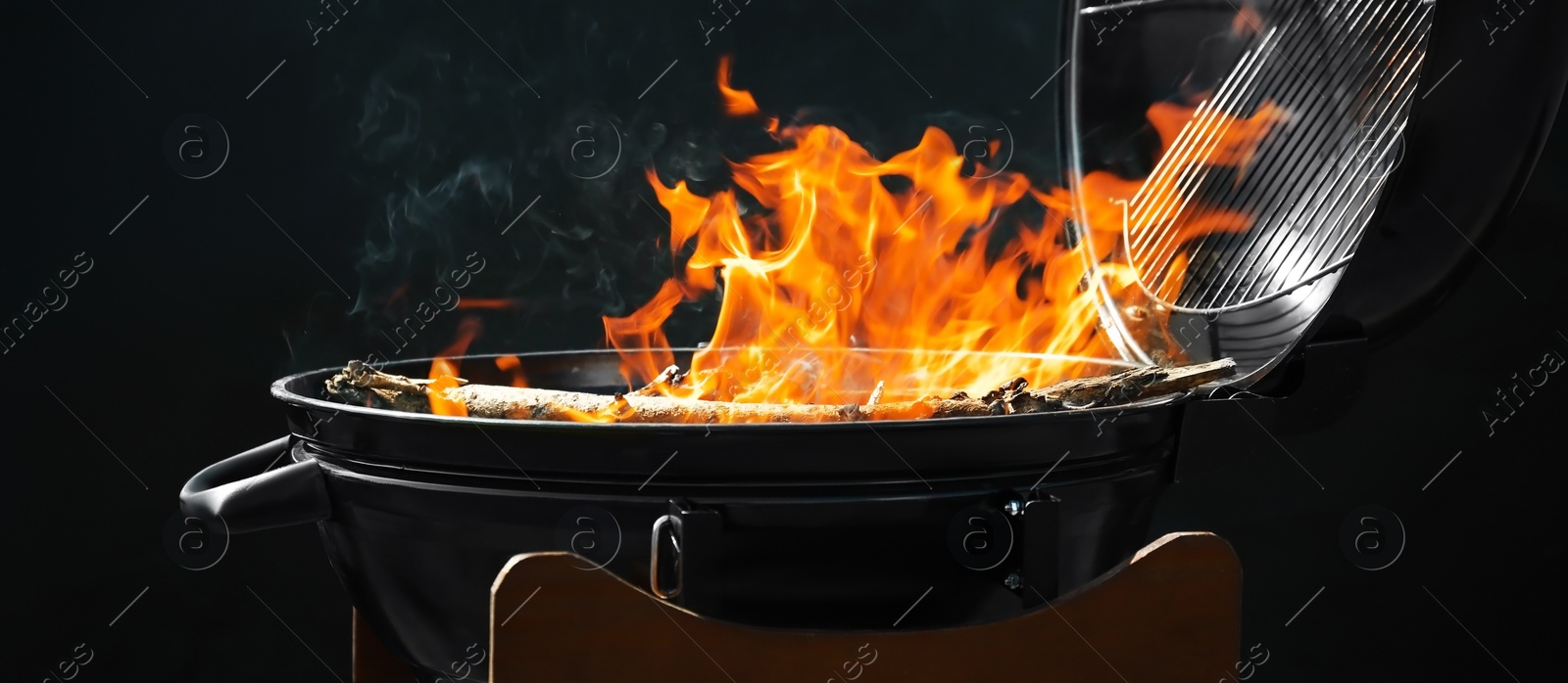 Image of New modern barbecue grill with burning firewood on dark background. Banner design