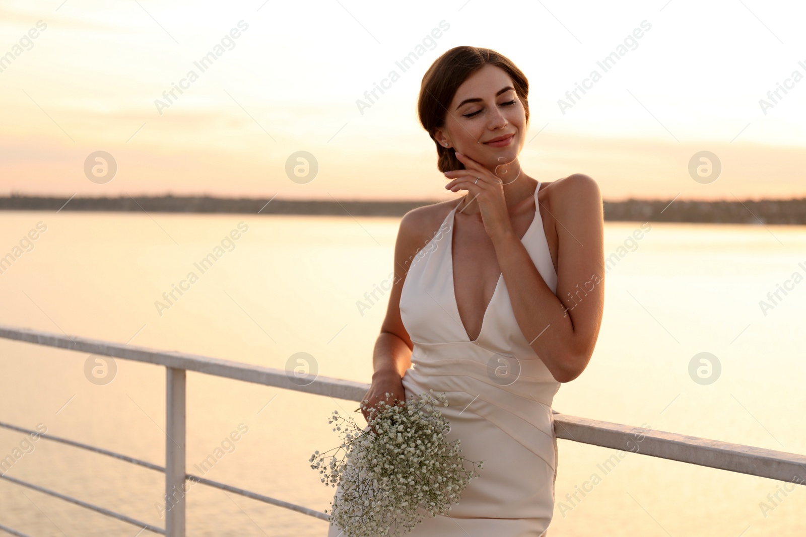 Photo of Gorgeous bride in beautiful wedding dress with bouquet near river on sunset