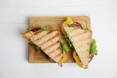 Wooden board with tasty sandwiches on white table, top view