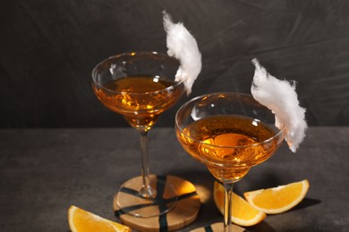 Photo of Tasty cocktails in glasses decorated with cotton candy and orange slices on gray table, closeup