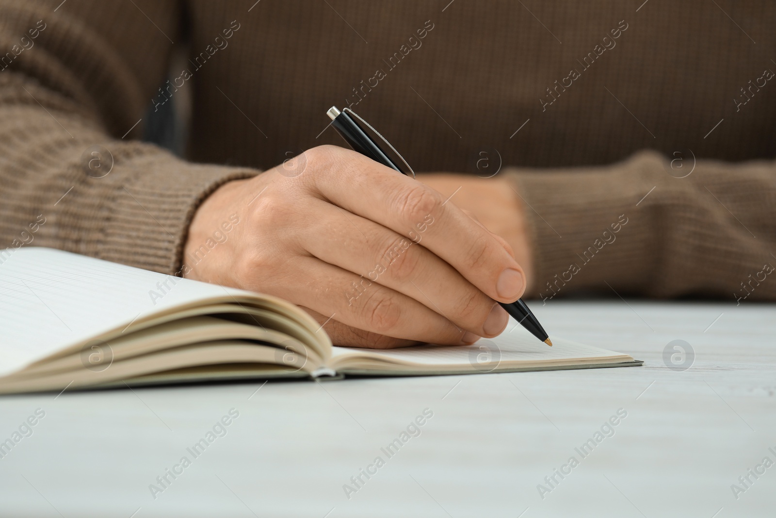 Photo of Man writing in notebook at white table, closeup