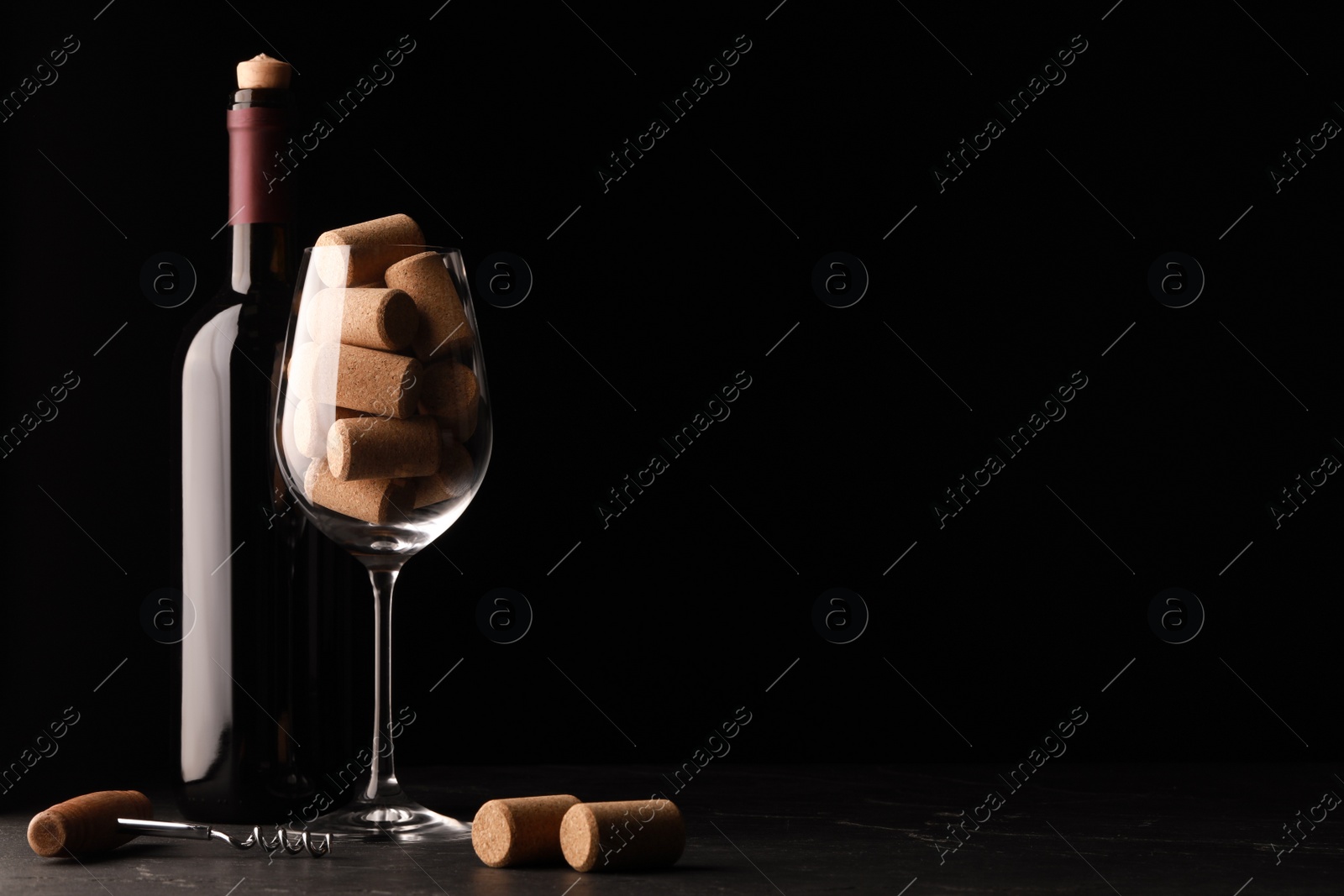 Photo of Bottle of wine, glass with corks and corkscrew on dark table. Space for text