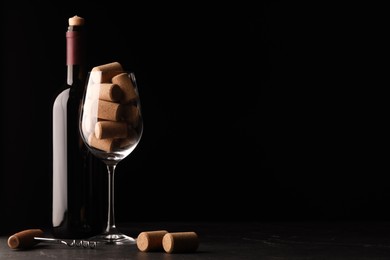 Bottle of wine, glass with corks and corkscrew on dark table. Space for text
