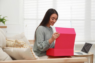 Happy young woman opening parcel at home. Internet shopping