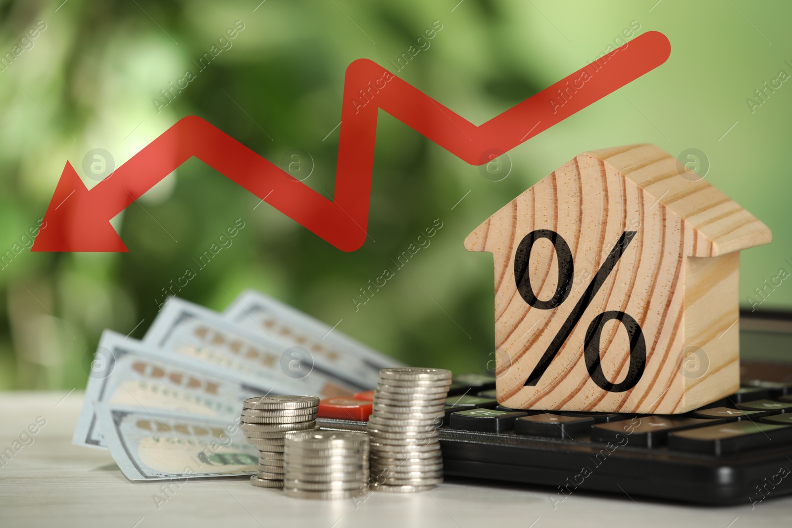 Image of Mortgage rate falling illustrated by downward arrow and percent sign. House model, money and calculator on table