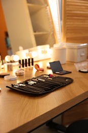 Photo of Set of makeup brushes and cosmetics on wooden table in room