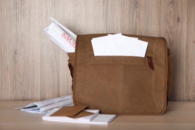Photo of Postman's bag full of letters and newspapers on wooden background