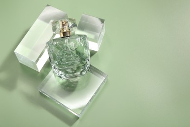 Stylish presentation of luxury perfume in sunlight on olive background, above view. Space for text