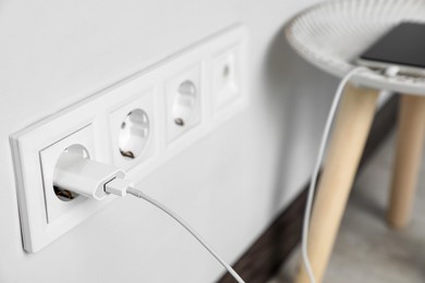 Modern smartphone charging from electric socket indoors, closeup. Space for text