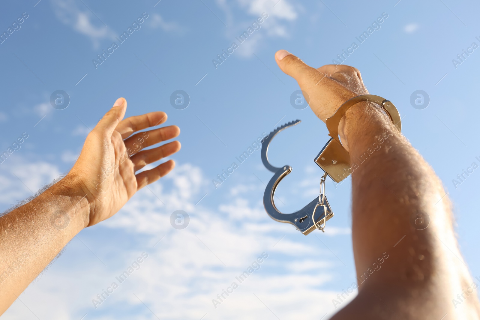 Photo of Man in handcuffs against blue sky outdoors, closeup