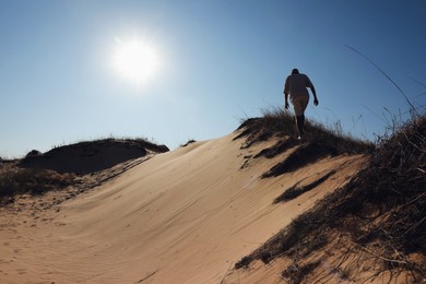 Photo of Man walking through desert on sunny day, back view