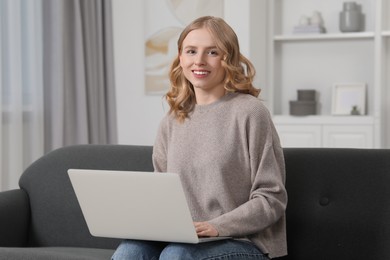 Beautiful woman with blonde hair using laptop on sofa at home