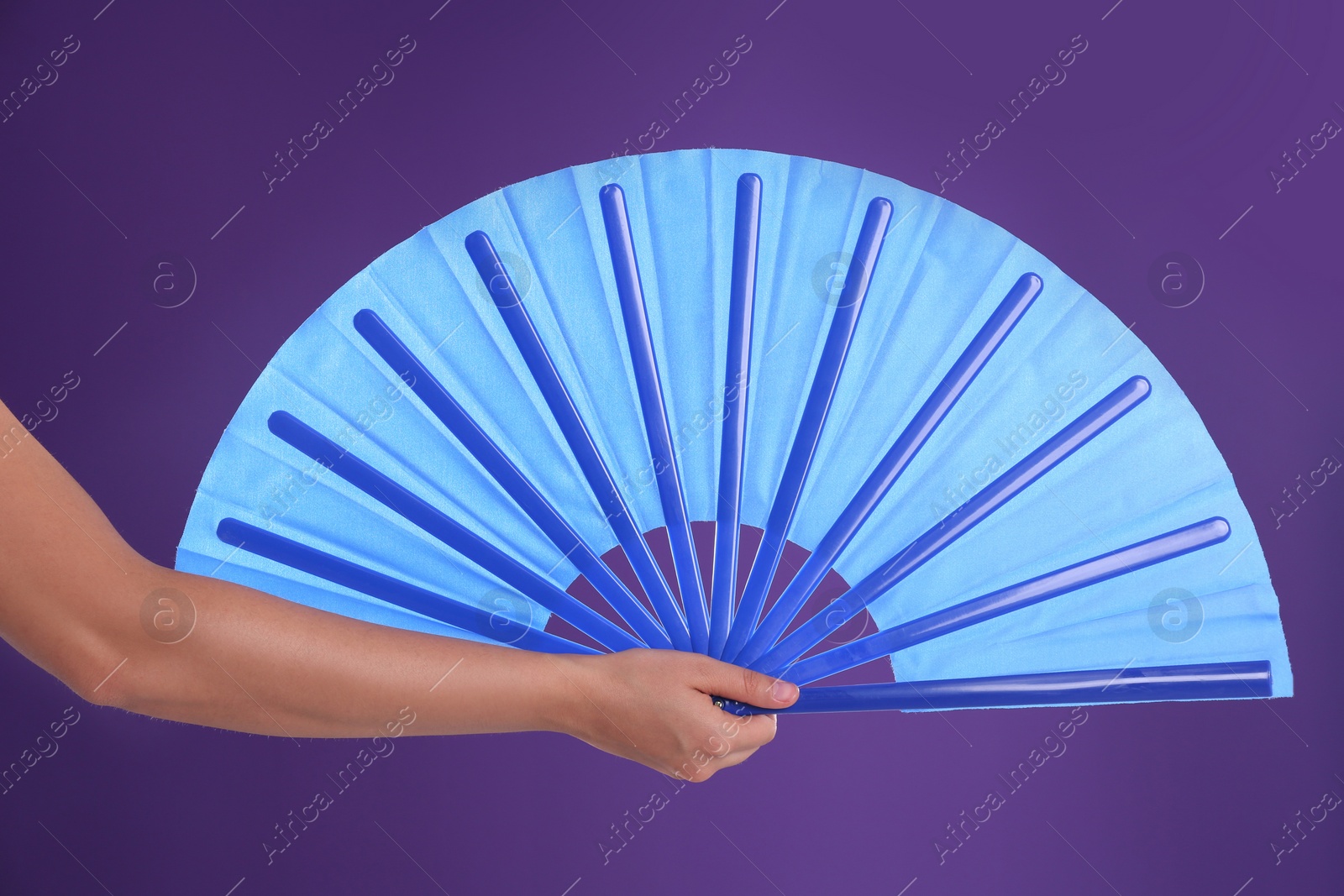 Photo of Woman holding blue hand fan on purple background, closeup