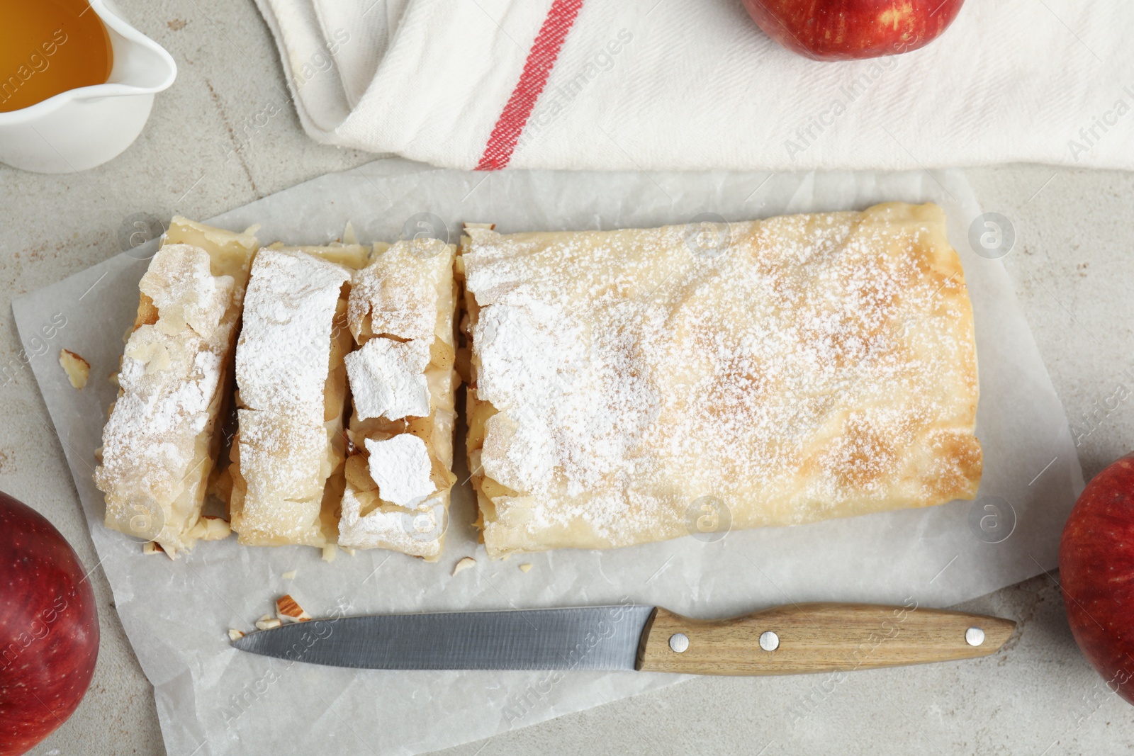 Photo of Delicious strudel, knife and fresh apples on light grey table, flat lay