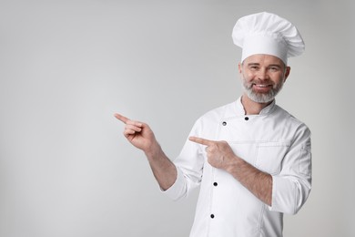 Photo of Happy chef in uniform pointing at something on grey background, space for text