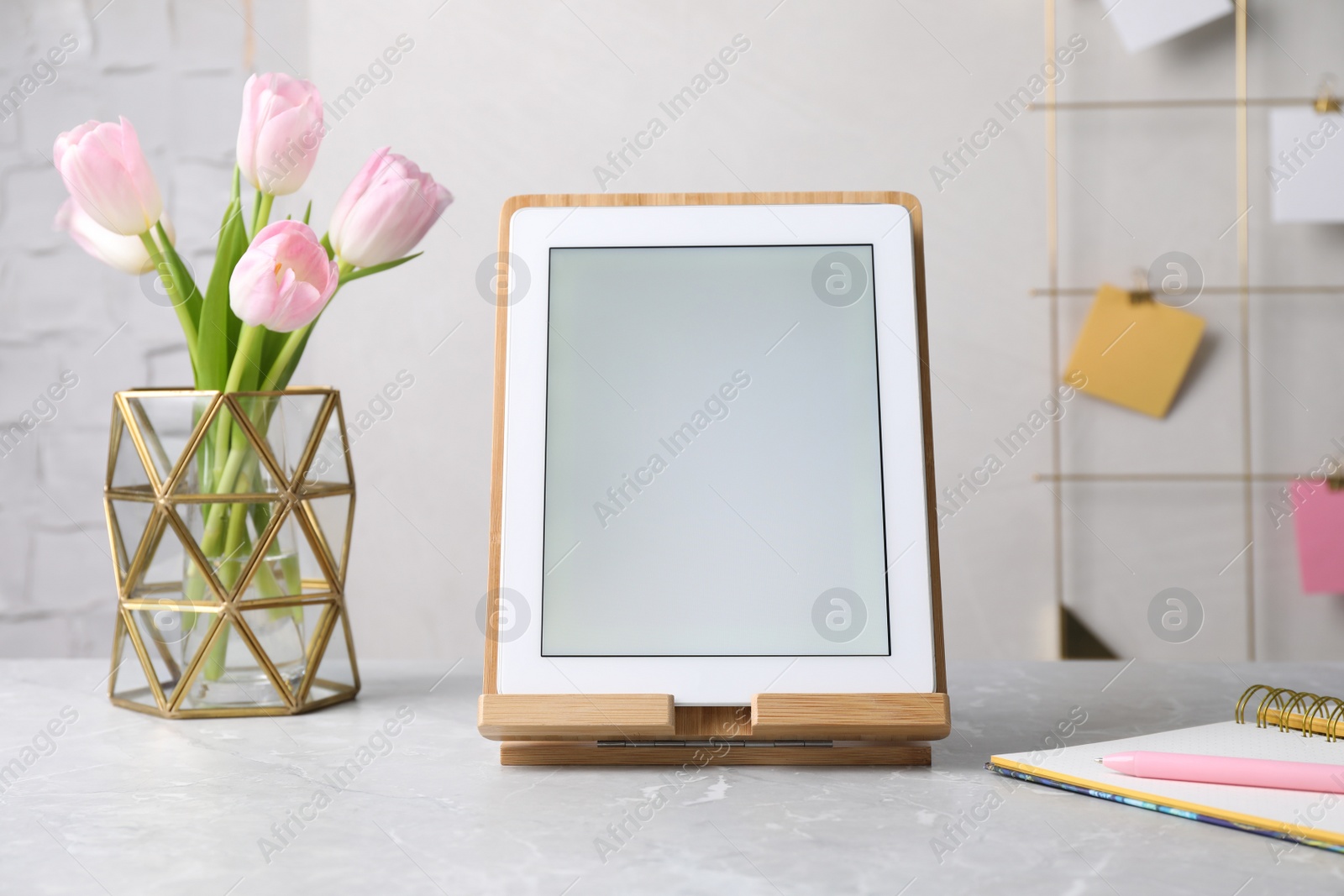 Photo of Modern tablet, stationery and flowers on grey marble table. Space for text