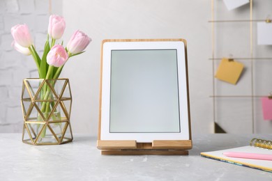 Photo of Modern tablet, stationery and flowers on grey marble table. Space for text